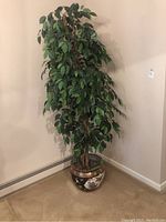 Full view of the faux ficus tree standing in the decorative pot against a beige wall and carpet floor.
