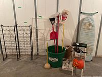 Photo of the metal step stool with padded top, ironing board, large green plastic tub containing cleaning tools, two black metal racks, and Halloween decorations including pumpkin lantern and spider.