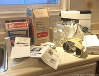 Kenwood Chef kitchen mixer accessories including mincer and liquidizer attachments, instruction manuals, original boxes on a countertop.