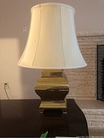 Full view of brass-like lamp with white fabric shade on a dark wood surface showing lamp shape and shade size.
