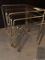 Three nesting tables with glass tops on gold-tone metal frames, arranged nested together.