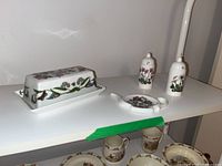 Butter dish, teabag rest, salt and pepper shakers on white shelf, showing full set.