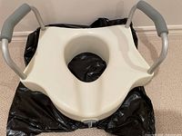 Top-down view of an off-white raised toilet seat with two grey foam-padded metal support handles.