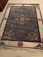 Full view of fringed throw rug with floral and circular design, cream border, and red circular motifs