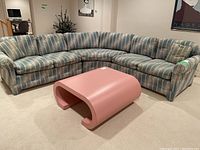 Front and side view of three-piece sectional couch with blue and gray striped upholstery and pink modern coffee table in front.