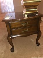 Front view of wooden side table with two drawers and brass handles, showing curved cabriole legs and polished medium brown wood finish.