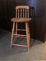 Full view of antique wooden spindle back stool showing overall shape and condition.