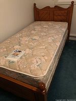 Full view of twin bed assembled with floral patterned Sealy mattress and box spring on wooden bed frame with carved headboard and footboard.