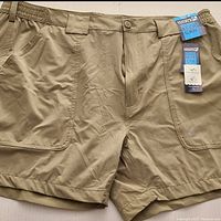 Front view of tan/beige Hook & Tackle Beer Can Stretch Shorts with visible tags indicating size 40 and showing front pockets and waistband detail.