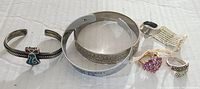 Full view of assorted silver and gold-toned bracelets and rings arranged on white surface.