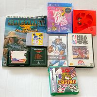 Top view of grouped video games showing SOCOM II with manual, Just Dance 2020 PS4, PC games Madden 06 and NBA Live 95, Atari and Nintendo 64 cartridges, plus Gameboy Advance boxed game