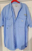 Front view of light blue Columbia fishing shirt showing button closure, multiple pockets, and collar