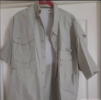 Front view of beige Columbia PFG fishing shirt hung on a door, showing overall size and structure including collar, buttons, and pocket placements.