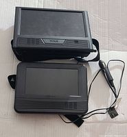 Two black RCA portable DVD player screens with straps and car power adapter cable visible, placed on a flat surface.