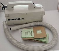 Photo of Oreck XL canister vacuum cleaner body with attached hose and manuals and vacuum bags placed next to it.