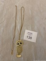 Two gold necklaces displayed on fabric background with auction lot card