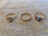 Three gold rings displayed side by side on white fabric