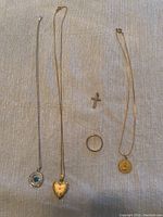 two necklaces displayed on fabric: white gold birthstone pendant and yellow gold heart locket pendant