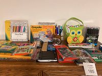 Photo showing a broad view of the lot on a table with crayons, pencil crayons, colouring books, Creative Lettering set by Crayola, and an owl-shaped container with markers.