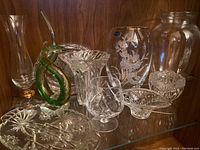 Photo showing various crystal and glass baskets, vases, and decorative bowls on a wooden shelf.