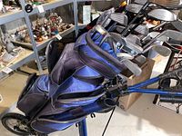 Golf cart holding golf bag with multiple golf clubs, displayed on concrete floor with surrounding shelves