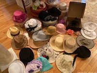 Overview of large collection of ladies hats including sun hats and dress hats in various styles, colors, and materials, displayed on the floor near decorative and original hat boxes.