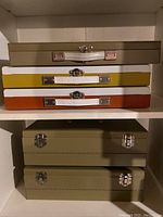 Five metal cases stacked in a shelf, showing varied colors and metal clasps