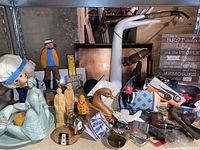 Wide view of assorted vintage knick knacks including figurines, cigar pipes, lighters, and decorative items on a table and shelf