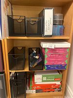 Shelving unit with assorted office supplies including paper, CDs, and mesh organizers.