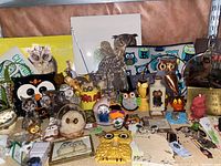 Shelf with a mixture of owl decor including figurines, framed prints, ceramic dishes, and owl-themed puzzle.