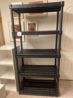 Full view of one black resin shelving unit showing five slatted shelves and sturdy posts.
