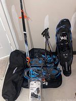 Photo showing two sets of snowshoes, two pairs of trekking poles and two black carry bags on floor.