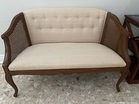 Full front view of the upholstered bench showing wooden frame, cane sides, and beige upholstery.