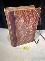 Three-quarter view of the antique book showing marbled paper board cover and leather spine.