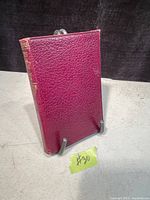 Closed front cover of maroon leather book standing vertically on a stand, showing textured leather surface and spine detailing.