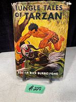 Front cover of Jungle Tales of Tarzan book showing illustrated dust jacket with Tarzan in a leopard loincloth fighting a tribal warrior with spear and shield.