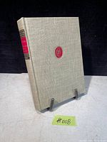 Front cover of the antique book showing beige cloth binding with red and black spine label and red monogram on front