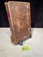 Front cover of the antique book showing heavily worn brown leather binding with red spine label.