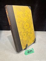 Antique hardcover book with yellow floral pattern and black spine standing on a table.