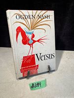 Front cover of 'Versus' showing red bird design on white dust jacket with title and author name.