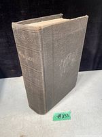 Photo of the closed hardcover antique book showing dark cloth with embossed designs and title text faintly visible