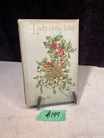 Front cover of the antique book Lady of the Lake by Walter Scott showing embossed and colored holly leaves and berries on pale green cover.