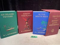 Set of three hardcover vintage books with green, red, and blue covers and a burgundy slipcase.