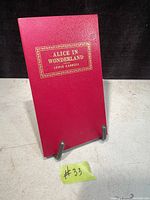Front red hardcover of vintage book 'Alice in Wonderland' by Lewis Carroll with gold embossed title and author name.