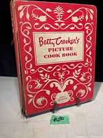 Front cover showing red hardback with white floral designs and title label 'Betty Crocker's Picture Cook Book'