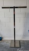 Full view of a chrome retail clothing rack with rectangular base and adjustable vertical pole.