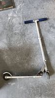 Full view of the scooter showing the silver frame and blue handle grips on a concrete floor surface