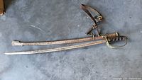 Full view of metal antique/vintage curved sword and rusted scabbard with leather strap on concrete floor