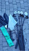 All light stands, umbrellas, LED bulbs, and green screen backdrop shown on stone tile surface, items assembled and laid out.