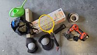 Full overview photo of all items showing power drill, watering can, tape, knee pads, flashlight, drop cloth box, fly swatter, and shower curtain bag.